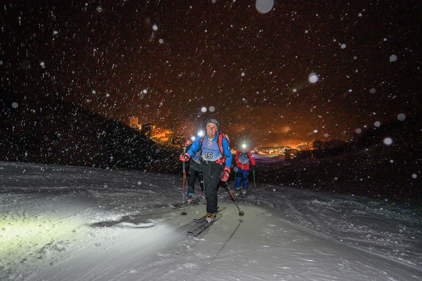 Skieurs dans la montée sous la neige, lumières de la station en contrebas