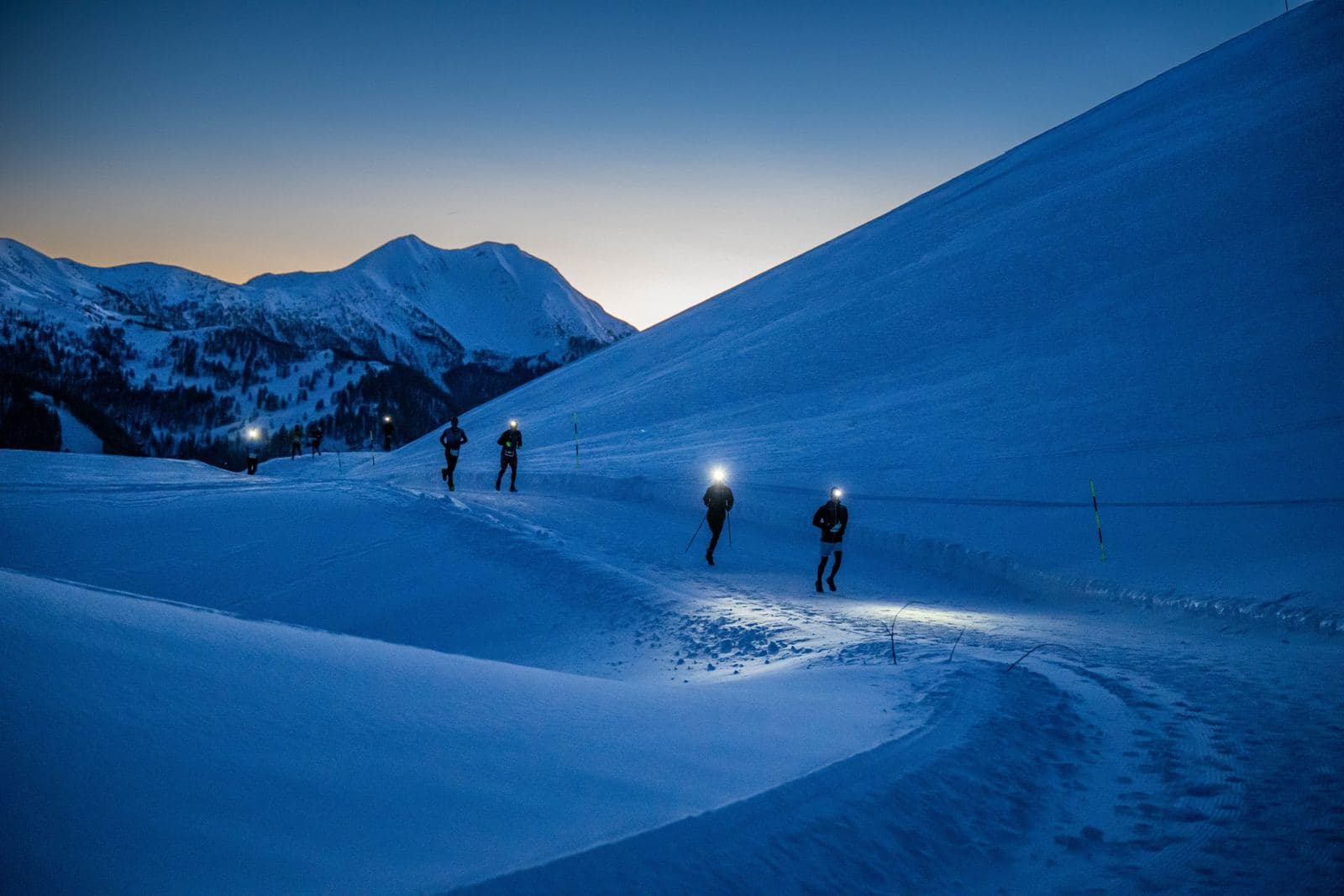 File de frontales dans un vallon enneigé à la tombée de la nuit